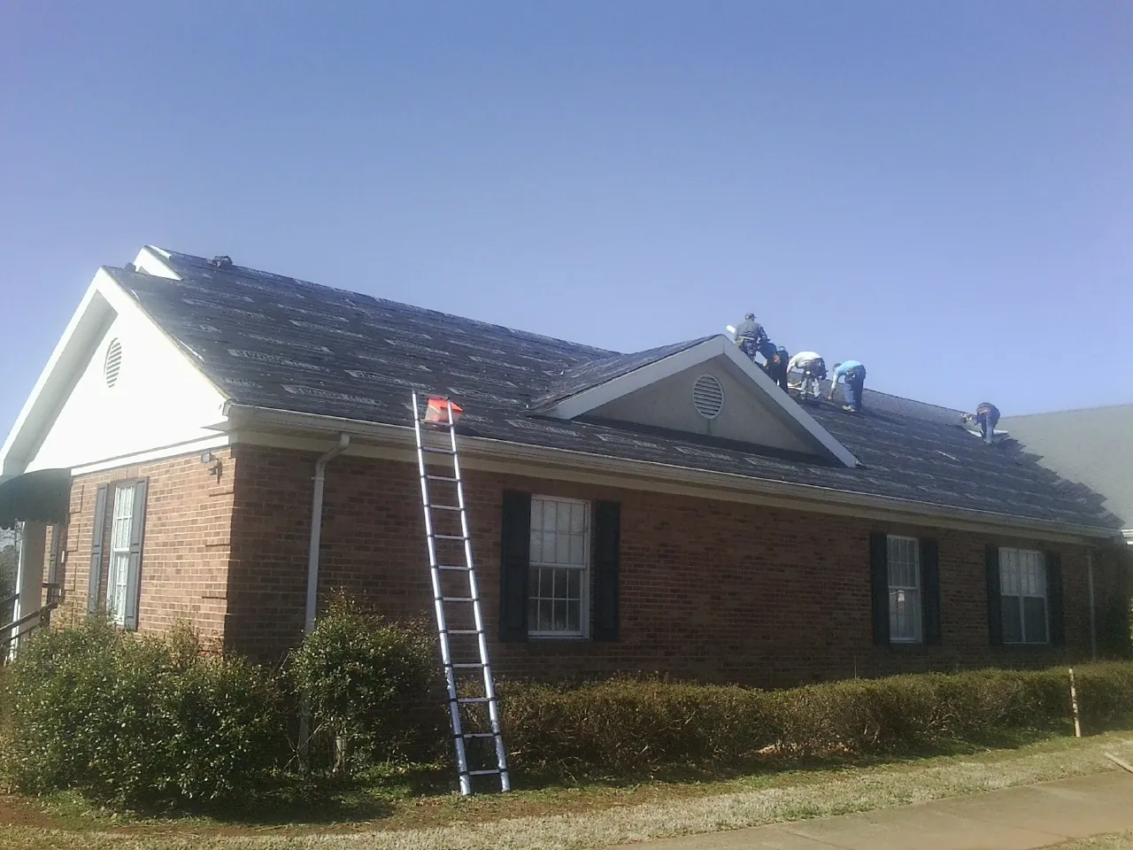 Crew tearing shingles off a brick ranch roof with a ladder set — Metal Roof Repair work by our crew in Wrightstown