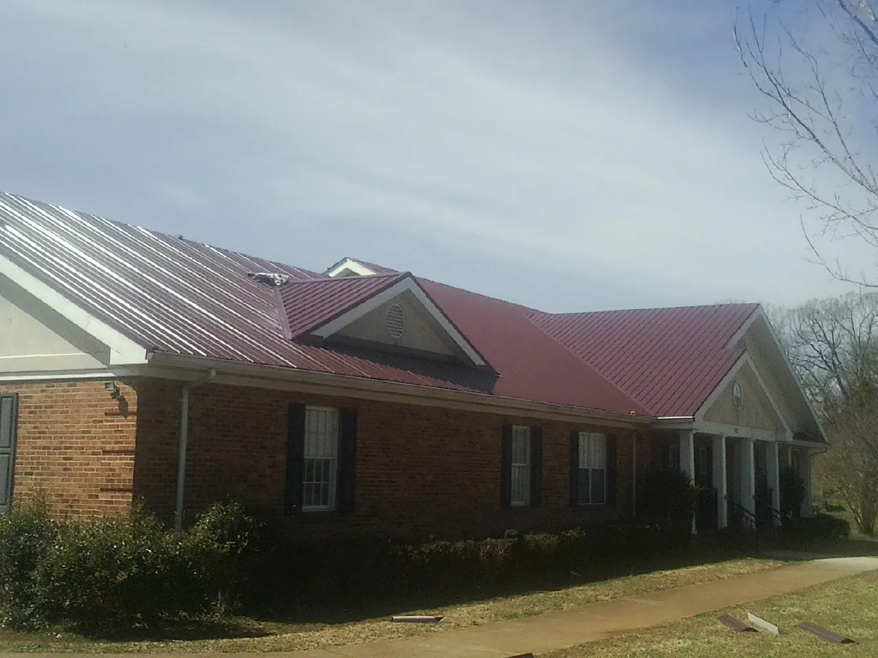 Red metal roof with gabled entries on a long brick building, from a Hail Damage Roof Repair job in Wrightstown