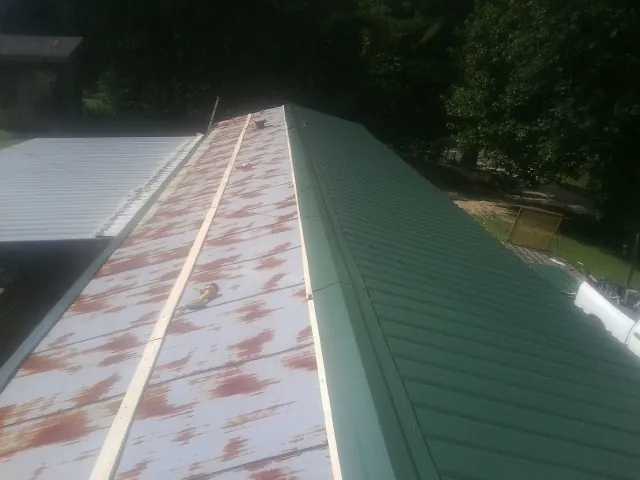 Old rusted panels beside newly installed green metal roofing — Wind Damage Roof Repair by Roofing Brothers in Wrightstown