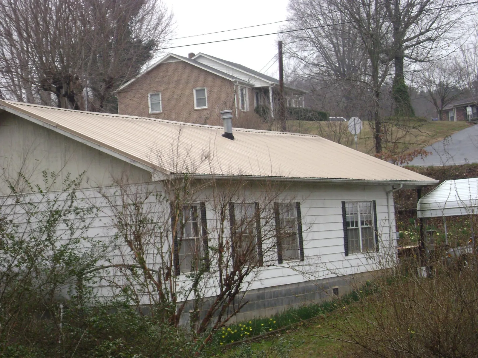Tan metal roof on a white sided house set into a hillside — Commercial Roofing by Roofing Brothers in Wrightstown